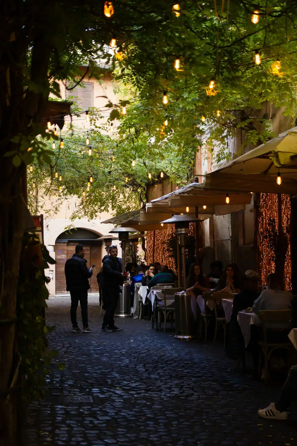 A lamplit street lined with restaurant tables at night