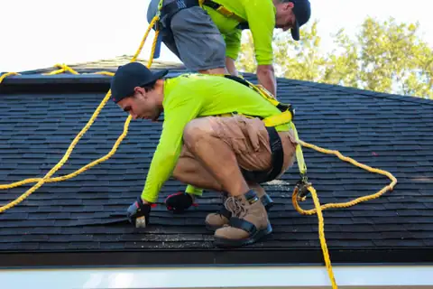 A roofer tied off on a steep shingle roof